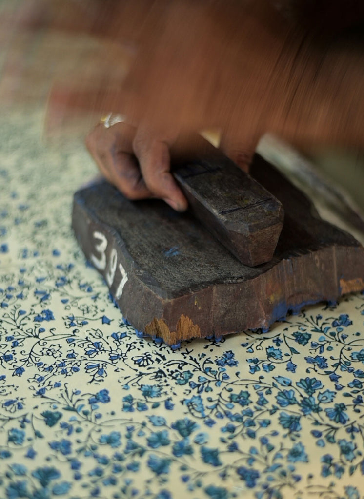 A wooden block printing blue and green patterns onto a yellow silk fabric 
