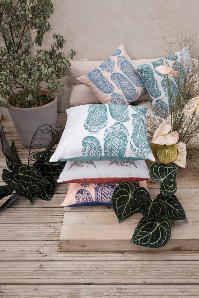 Garden with outside seating with colourful block printed linen cushions on it, coloured beige, green, blue, purple and pink surrounded by flowers and trees.