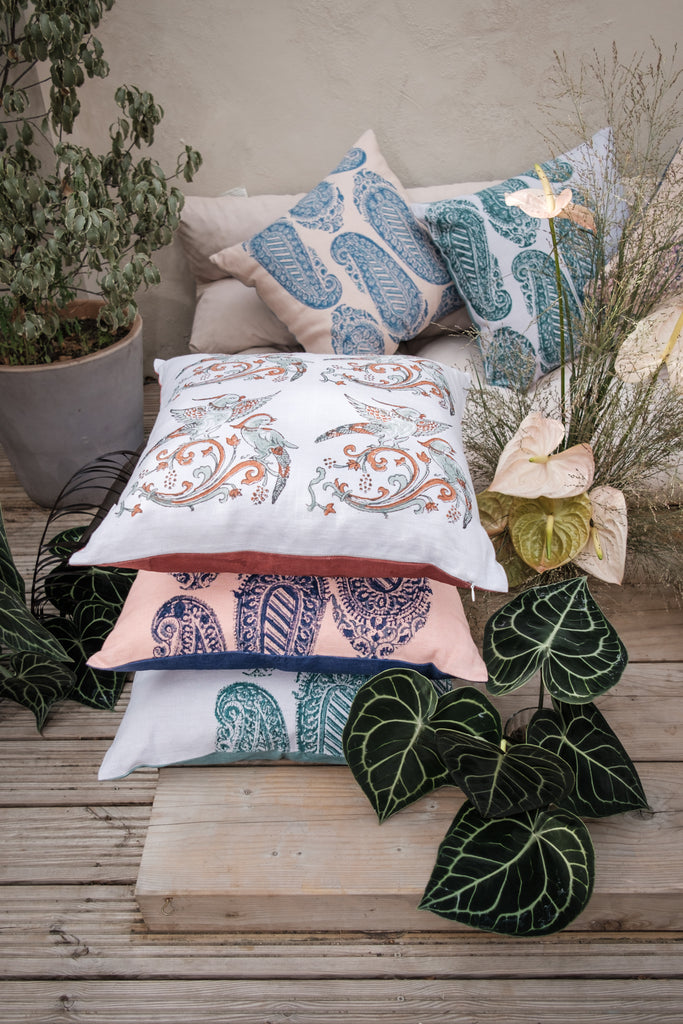 Garden with outside seating with colourful block printed linen cushions on it, coloured purple, green, red, blue and pink surrounded by flowers and trees.