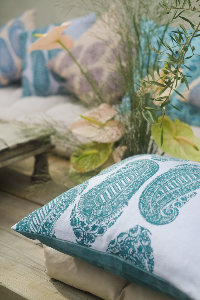 Close up of linen cushion in a garden, block printed with green, blue and purple colours with plants. 