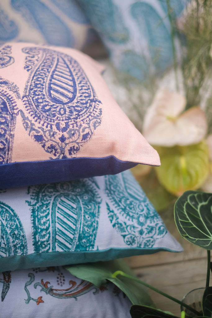 Close up on colourful block printed linen cushions, coloured beige, green, blue, purple and red surrounded by plants