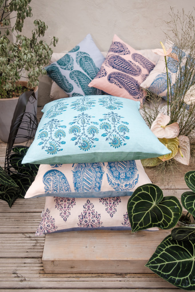 Garden with outside seating with colourful block printed blue, pink and beige linen cushions and flowers and trees.