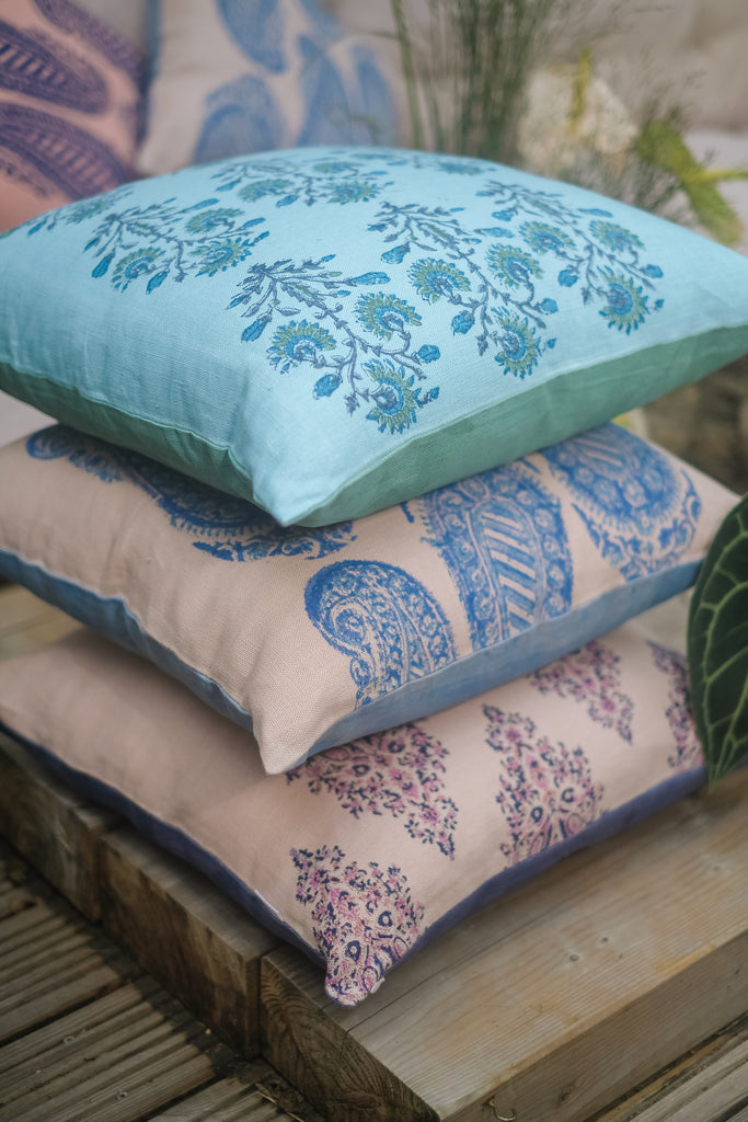 Garden with outside seating with colourful block printed blue, pink and beige linen cushions and flowers and trees.