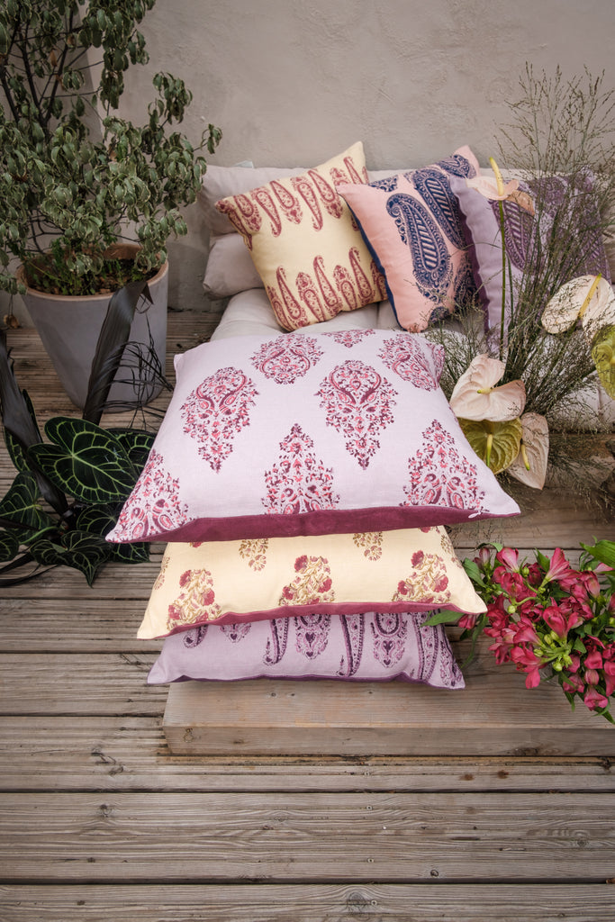 Garden with outside seating with colourful block printed linen cushions on it, coloured yellow pink purple red, surrounded by flowers and trees.