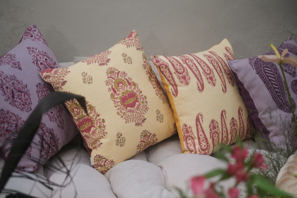 Seating with colourful block printed linen cushions on it in yellow pink purple red, surrounded by plants