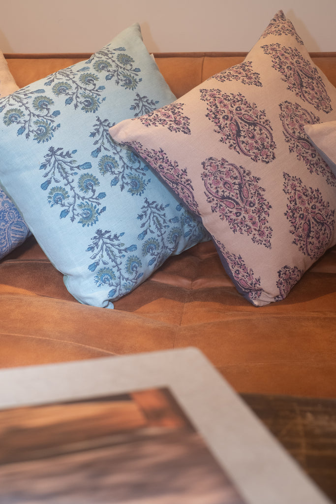 Blue, pink and beige block printed linen cushions sit on a brown leather sofa.